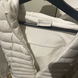 Vit pufferjacka med huva  - Snygg vit pufferjacka med huva och dragkedja framtill. Jackan har quiltad framsida, två fickor med dragkedja och en extra ficka på ärmen. Mjuk bomullsmix på ärmar och rygg, perfekt för dig som gillar stilren och clean look. Fråga gärna.