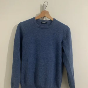 Blå stickad tröja från J.Lindeberg - Snygg blå stickad tröja från J.Lindeberg i storlek Xl i barn storlek som motsvarar Size S i vanlig storlek. Tröjan har rund hals och långa ärmar, perfekt för dig som gillar enkel och stilren design. Materialet är mjukt och skönt, passar bra till jeans eller chinos.