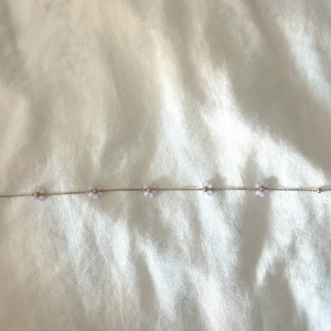 Guldhalsband  - Superfint halsband med tunn guldfärgad kedja och små rosa blommor av pärlor jämnt utspridda längs kedjan, justerbar längd med karbinlås (stainless steel)