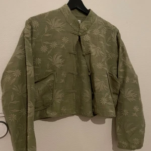 Broderad grön kofta i japansk stil  - Säljer en grön gullig kofta köpt i japan. Den har traditionella knytknappar framtill, två fickor och en croppad passform. Riktigt snygg till kostymbyxor eller jeans. Säljer då den inte används. Något lös passform, strl M/L och färgen är lite ljusare mer som på bild 2