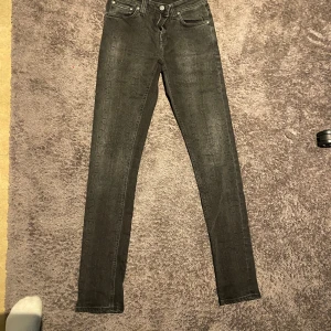 Svarta jeans från Nudie Jeans - Säljer ett par svarta skinny jeans från Nudie Jeans i storlek 27/32. Jeansen har ett diskret ormmönster och klassisk femficksdesign. Materialet är stretchigt och bekvämt.