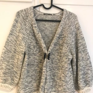 Gråmelerad kofta från Zero - Säljer en blå/vit stickad kofta från Zero i storlek 36. Jättefin och sparsamt använd. Perfekt att slänga över ett linne eller t-shirt för en mysig outfit. 