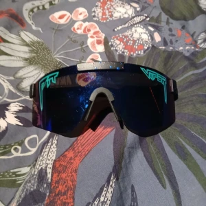 Blå Viper sportglasögon med spegeleffekt - Säljer ett par riktigt feta Viper sportglasögon med blå spegelglas och svarta detaljer. Glasögonen har en futuristisk, kantig form och coola turkosa Viper-loggor på sidorna. Bågen är svart med silverfärgade detaljer och små färgprickar på ovansidan för extra stil.