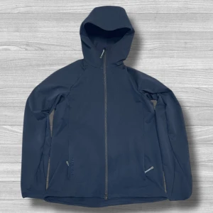 Mörkblå Houdini Daybreak vindjacka XS - Snygg mörkblå Houdini Daybreak vindjacka i dammodell med huva och hel dragkedja framtill. Jackan har två sidofickor med diskreta detaljer och är tillverkad av polyester och polyamid. Perfekt för dig som gillar outdoor och vill ha en stilren look.