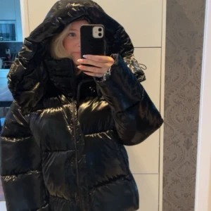 Svart pufferjacka från Calvin Klein Jeans - Säljer en svart, glansig pufferjacka från Calvin Klein Jeans med stor huva och dragkedja framtill. Logga på insidan och högra bröstet. Perfekt för kalla dagar och har en riktigt oversized vibe. Den är super varm!!