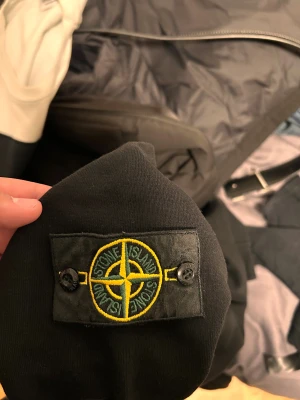 Svart Stone Island sweatshirt S - Svart sweatshirt från Stone Island i storlek S. Tröjan har det klassiska broderade Stone Island-emblemet på ärmen och en stor logga framtill. Mjuk bomullskvalitet och rund hals. Perfekt för dig som gillar streetwear och vill ha en clean look.