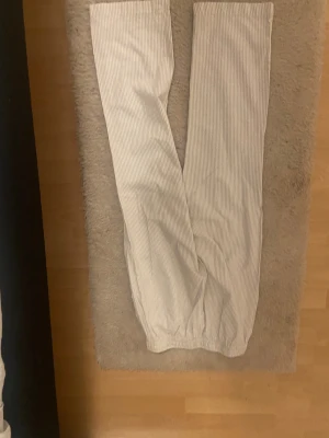 Randiga linnebyxor från 157 XS - Snygga ljusbeige linnebyxor från 157 i storlek XS. Byxorna har tunna vertikala ränder i vitt och beige, elastisk midja med snörning och raka ben. Perfekta för chill dagar och har en skön, luftig känsla tack vare linnematerialet.