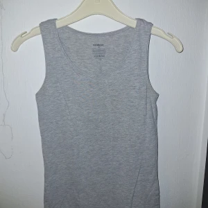 Grå linnetopp - Säljer en basic grå linnetopp från Newbody i storlek XS. Toppen är ärmlös med rund halsringning och har en mjuk och stretchig känsla. Perfekt att styla med jeans eller shorts för en clean look.