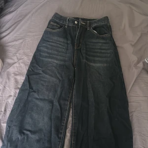 Mörkblå wide baggy jeans  - Säljer ett par mörkblå jeans med bred passform och tydliga kontrastsömmar. Jeansen har klassisk femficksdesign, låg midja och coola slitningar över låren. Perfekta för dig som gillar en avslappnad och trendig look. Urban Outfitters 