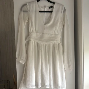 Vit klänning från Bubbleroom - Superfin vit kortklänning från Bubbleroom i storlek 34 med v-ringning, långa transparenta ärmar. Klänningen har knytband i ryggen. Perfekt för tex student. Knappt använd. Köpte den till min student men då jag hittade en annan klänning så blev det att denna bara fick hänga. Använd enstaka gång. Den är som ny. Original pris 699kr