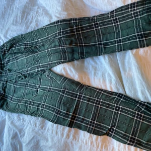 Gröna rutiga byxor från H&M - Snygga gröna byxor från H&M med vitt och svart rutmönster. De har avslappnad passform och är tillverkade i mjukt bomullstyg, perfekta för en chill och trendig look. Resår i midjan för extra komfort.