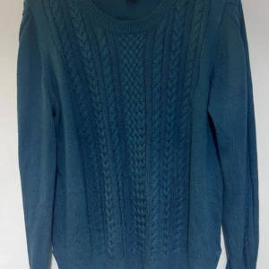 Blå stickad tröja från Lindex XL - Mysig blå stickad tröja från Lindex i storlek XL. Tröjan har ett snyggt flätmönster framtill och rund halsringning. Perfekt för kyliga dagar och enkel att matcha med jeans eller kjol.