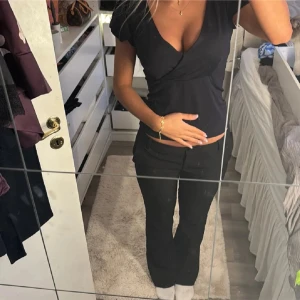 Svart omlottopp med v-ringning - Säljer en svart omlottopp med djup v-ringning och korta, lätt volangiga ärmar. Toppen har en figurnära passform och är tillverkad i ett mjukt bomullsliknande material. Perfekt att styla med jeans eller kjol för en trendig look.