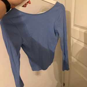 Ljusblå långärmad topp med v-ringning i ryggen  - Säljer en ljusblå långärmad topp med djup v-ringning baktill. Toppen är i mjuk bomull och har en enkel, stilren design som passar perfekt till jeans eller kjol. Den är figurnära och har en klassisk look.
