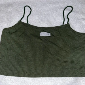 Olivgrön ribbad linnetopp - Säljer en olivgrön ribbad linnetopp från The Time For Change. Toppen har smala axelband och är croppad, perfekt för varma dagar. Materialet är mjukt och stretchigt för en bekväm passform.