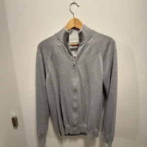 Grå  zip tröja - Säljer en stilren grå tröja från MNG med half zip och hög krage. Tröjan har långa ärmar, ribbade muddar och är tillverkad i mjukt bomullsmaterial. Perfekt för lager-på-lager och chill vardagsstil.