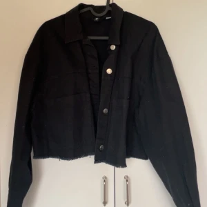 Svart croppad jeansjacka från H&M - Svart croppad jeansjacka från H&M med silverfärgade knappar framtill och vid ärmsluten. 