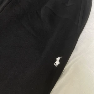 Polo Byxor - Svarta mjukisbyxor från Ralph Lauren med klassisk vit broderad logga på låret. Byxorna har en enkel och stilren design, perfekta för en chill och avslappnad look. Tillverkade i mjukt material för extra komfort.