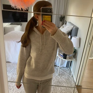 Beige stickad hoodie från Gina Tricot - Mysig beige stickad hoodie från Gina Tricot med huva och snörning. Tröjan har ribbade muddar och nederkant, samt lång ärm. Perfekt för dig som gillar en chill och enkel stil.