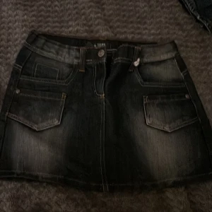 Svart jeanskjol från Teens Girls - Cool svart jeanskjol från Teens Girls med slitna detaljer och kontrastsömmar. Kjolen har klassiska fem fickor, bälteshällor och knappstängning framtill. Snyggt tvättad denim med en kort passform som ger en trendig look.