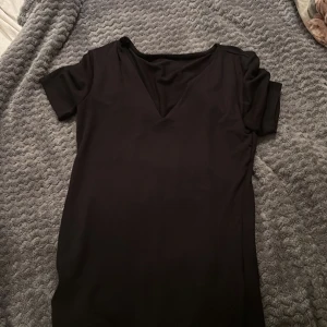 Svart kortklänning med v-ringning - En stilren svart kortklänning med v-ringad hals och korta ärmar. Klänningen har en enkel och klassisk design som gör den lätt att matcha med accessoarer. Perfekt för dig som gillar minimalistisk stil.