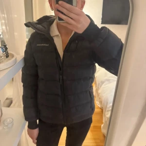 Svart pufferjacka Peak Performance - Säljer en svart pufferjacka från Peak Performance med huva och dragkedja. Jackan har en quiltad design, logga på bröstet och är tillverkad i syntetmaterial. Perfekt för kalla dagar! Passar till allt och inga effekter på den ❤️
