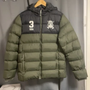 Grön och svart pufferjacka Vinson Polo Club - Säljer en grön och svart pufferjacka från Vinson Polo Club med huva och dragkedja. Jackan har tryck med klubbens logga och siffran 3 på bröstet. Fodrad och perfekt för kalla dagar, med två sidofickor och sportig look.