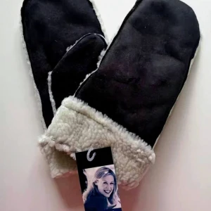 Svarta tumvantar från Emilia - Mysiga svarta tumvantar från Emilia med vit fluffig insida och kant. Utsidan är i mockaliknande material och insidan är mjuk och varm, perfekt för kalla dagar. Klassisk tumvante-modell med enkel design och snygg kontrast mellan svart och vitt.