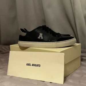 Svarta sneakers från Axel Arigato - Säljer ett par sjukt stilrena pjucks från Axel Arigato i läder med bokstaven A på sidan som en unik detalj. Perfekta för både vardag och fest! Även väldigt bra för kommande årstider då de även tål kyla. Skorna är i andvänt skick och allt og finns kvar. 