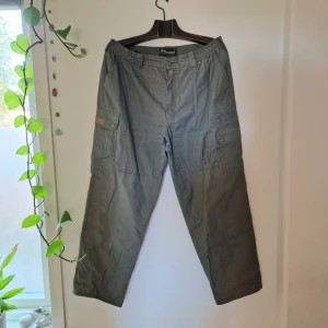 Friluftsbyxor  - Skogs-gröna friluftsbyxor i mjukt tyg (ej stretch) och resår i midjan. Mått: Ben - 100 cm, Midja (ihopdraget läge med resår) 45 cm. 