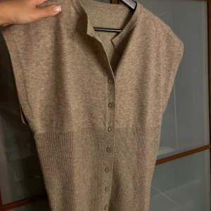 Beige stickad tröja med knappar - Snygg beige stickad tröja med ribbad nederdel och knappar framtill. Tröjan har en enkel, rak passform och går in lite tajtare i midjan.