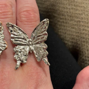 Silvrig ring med fjärilsdesign - Cool ring i form av en stor fjäril i silvrig metall. Fjärilen har en detaljerad och texturerad yta som ger ett unikt och trendigt intryck. Perfekt accessoar för dig som vill sticka ut och addera lite edge till din stil.