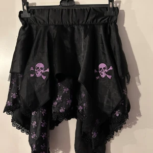 Kjol från Poizen. Storlek onesize. - Helt ny kjol från Poizen. Resår i midjan. Tryckta små döskallar på undertaket och broderade större döskallar på övertaget.