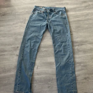 Levi's 501 ljusblå jeans W31 L34 - Klassiska Levi's 501 jeans i ljusblå denim. Rak passform med knappgylf och fem fickor. Snygga kontrastsömmar och ikonisk läderpatch bak i midjan. Perfekta för dig som gillar tidlös stil och vill ha ett par äkta Levi's Premium.