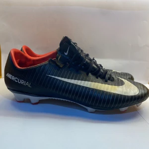 Nike Mercurial Vapor XI FG ” Pitch dark”  - Säljer ett par Nike Mercurial fotbollsskor i svart med vit swoosh och röda detaljer på insidan. Skorna har snörning och platt sula med dobbar för bra grepp på planen. Perfekt för dig som vill ha stil och funktion på fotbollsplanen.