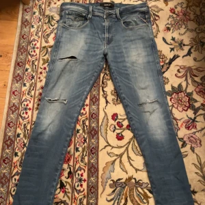 Replay ljusblå slitna jeans - Säljer ett par ljusblå jeans från Replay med slitna detaljer och hål på benen. Jeansen har klassisk femficksdesign, normal passform och raka ben. Materialet är mjukt denim som ger en avslappnad vibe. Hör av er vid funderingar✌️