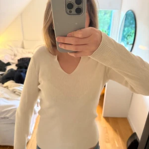Beige ribbad stickad tröja v-ringad - Säljer en beige stickad tröja med v-ringning och lång ärm. Tröjan är ribbad och har en slim passform som sitter snyggt på kroppen. 