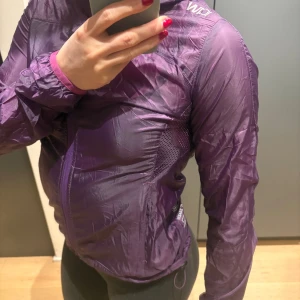 Lila vindjacka från ICANIWILL - Säljer en tunn och lätt lila vindjacka från ICANIWILL med huva och dragkedja framtill. Jackan har meshpaneler på sidorna för extra ventilation och är perfekt för löpning eller utomhusträning. Snygg sportig look och smidig passform. Aldrig använd säljer pga för liten! 
