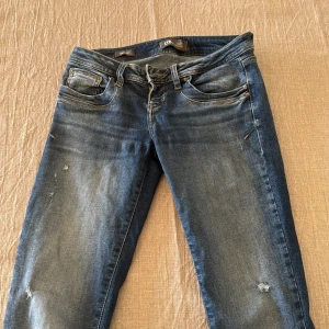 Blå jeans från LTB med slitningar - Säljer ett par blå jeans från LTB med snygga slitningar och tvättade detaljer. Klassisk femficksmodell med dragkedja och knapp. Jeansen har en rak passform och är tillverkade i jeansmaterial med lite stretch för extra komfort. Storleken är 27x36!