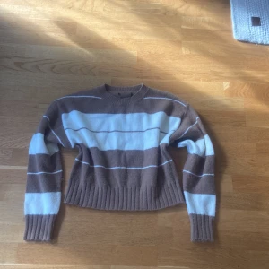 Randig brun och vit stickad tröja - Mysig stickad tröja med breda bruna och vita ränder. Tröjan har ribbad nederkant och ärmar, rund halsringning och lång ärm. Perfekt för chill dagar.