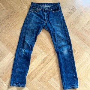 Levi's 505 blå jeans W31 L32 - Klassiska Levi's 505 jeans i blå denim med snyggt slitna detaljer. Vanlig passform, fem fickor och ikonisk läderpatch bak i midjan. Jeansen har normalhög midja och är tillverkade i robust bomullsjeans. Perfekta för en avslappnad och tidlös stil. Hör av er vid frågor