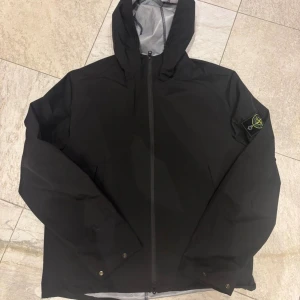 Svart vindjacka från Stone Island - Svart vindjacka från Stone Island. material som passar perfekt för blåsiga dagar. Enkel och stilren i st L 