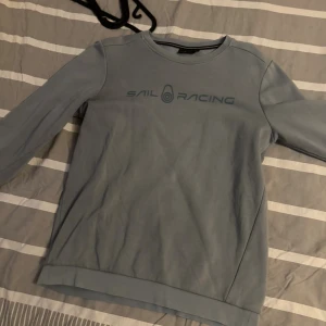 Blå Sail Racing sweatshirt i bomull - Snygg blå sweatshirt från Sail Racing med tryckt logga på bröstet och liten logga i nacken. Tröjan har rund hals, långa ärmar och är tillverkad i mjuk bomull med borstad insida för extra komfort.