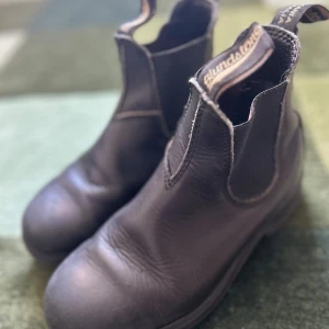 Svarta Blundstone chelsea boots - Klassiska svarta chelsea boots från Blundstone i robust skinn med elastiska paneler på sidorna och dragflikar fram och bak. Snygg rund tå och grov sula för extra grepp. Perfekta för dig som vill ha en tidlös och cool look.