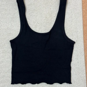Svart ribbat linne från Bik Bok - Svart ribbad linnetopp från Bik Bok i storlek S. Toppen är ärmlös med rundad halsringning och har en croppad passform med volanger nertill.