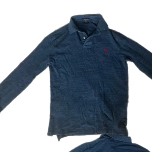 Mörkblå pikétröja från Ralph Lauren - Säljer en mörkblå långärmad pikétröja från Polo Ralph Lauren i custom fit. Klassisk krage, knappar vid halsen och den ikoniska röda loggan broderad på bröstet. Perfekt för dig som gillar stilrena och tidlösa plagg.