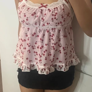 Rosa blommig linnetopp med spets - Supersöt rosa linnetopp med körsbärsmönster och vita spetsdetaljer vid halsen och midjan. Toppen har tunna axelband, små rosetter och volangkant längst ner. Perfekt för dig som gillar gulliga och lekfulla plagg med romantisk vibe.💕💕pris kan diskuteras