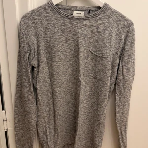 Gråmelerad långärmad tröja WinWin - Gråmelerad långärmad tröja från WinWin i 100% bomull. Tröjan har en enkel design med rund halsringning och en liten bröstficka. Perfekt för en chill och avslappnad stil. Storlek S.