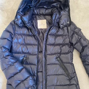 Midnight blue Moncler pufferjacka med huva - Snygg marinblå pufferjacka från Moncler med glansig finish och huva. Jackan har dragkedja framtill, två snedställda fickor med dragkedja och klassisk quiltad design. Perfekt för kalla dagar och riktigt stilren look. Den är äkta och bevis finns , i storlek 12 y men funkar som en xxs/xs också ! 