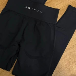 Svarta leggings från AWYROW - Svarta leggings från AWYROW med hög midja och bred resår för extra komfort. Perfekta för träning eller chill, med stilren logga framtill i vitt. Mjukt och stretchigt material som sitter skönt hela dagen.